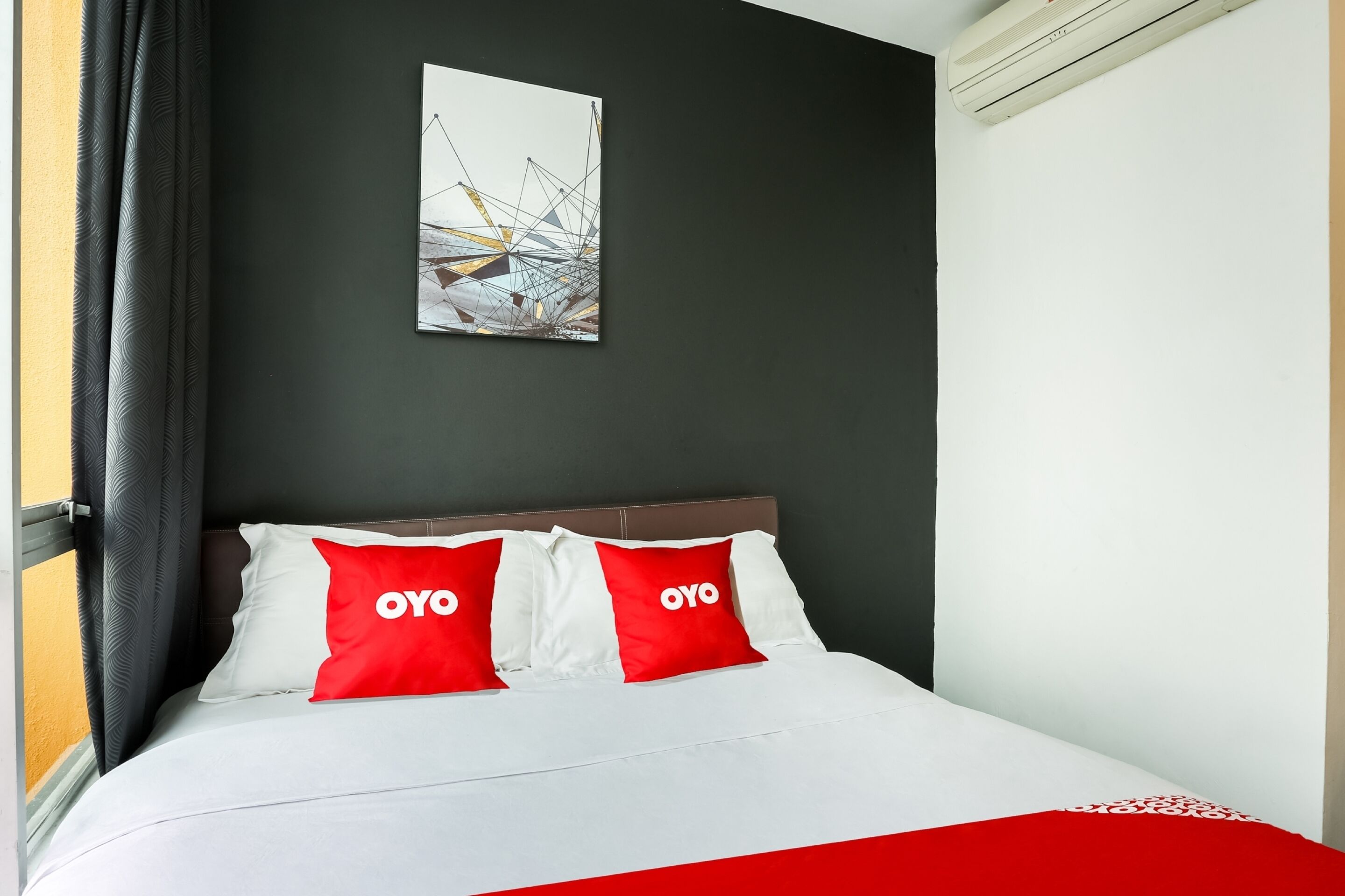 A hotel room with a bed, a painting on the wall, and a red and white bedspread.