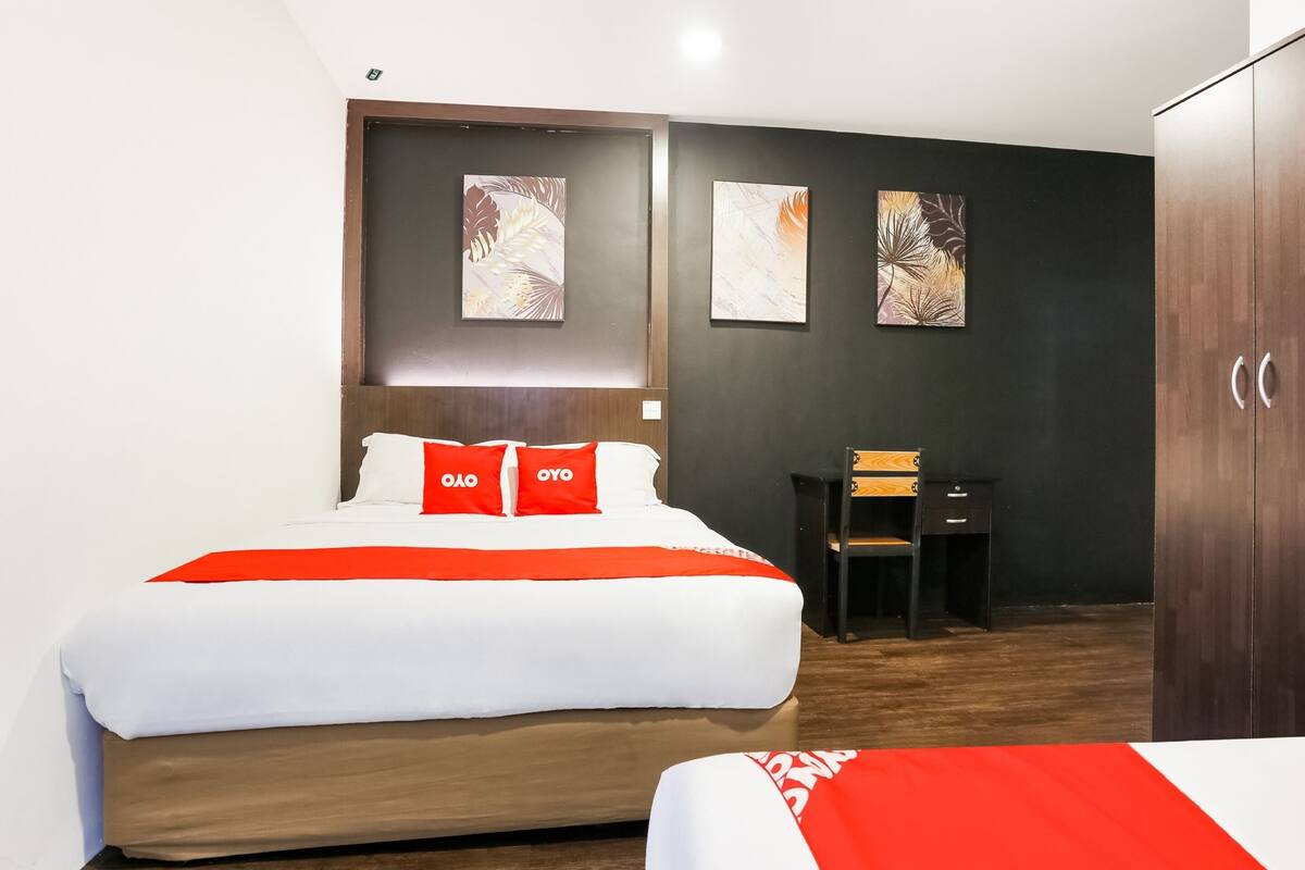 A hotel room with a large bed, a desk, and two artwork pieces on the wall.