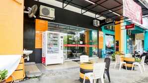 A hotel entrance with a glass door, a vending machine, and outdoor seating with chairs and a table.