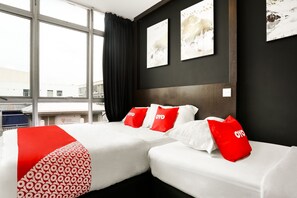 Hotellihuone, jossa on kaksi sänkyä, suuri ikkuna ja taideteoksia seinillä.