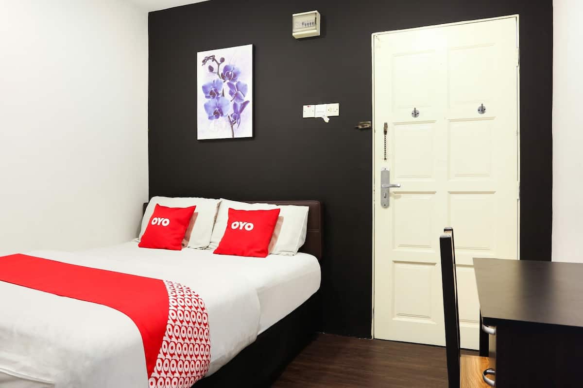 A hotel room with a bed, a desk, a door, and a wall-mounted light switch.