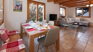 A cozy living room with a wooden ceiling, a dining area with a table set for two, and a sofa.