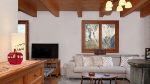 A living room with a wooden ceiling, a television, a sofa, and a window with a mountain view.