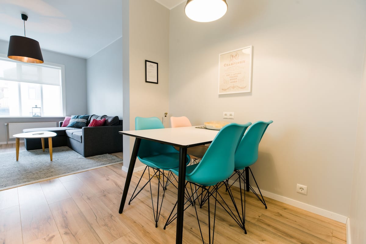 A modern living room with a dining area, featuring a sofa, a table, and teal chairs.