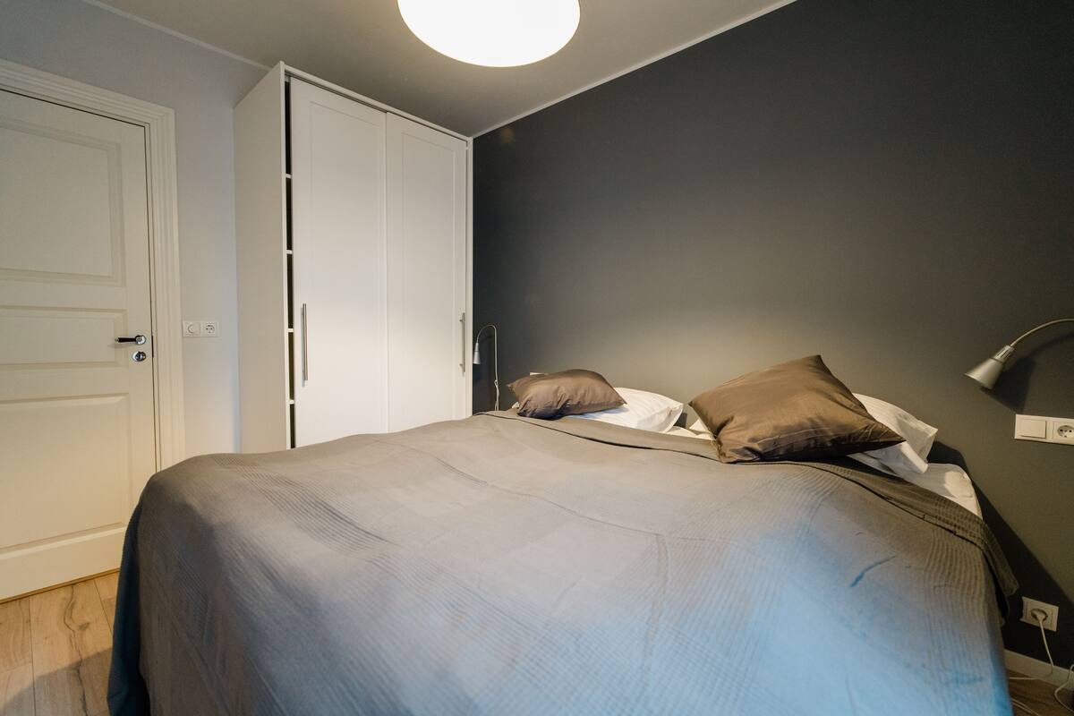 A bedroom with a bed, pillows, a bedside lamp, and a wardrobe.