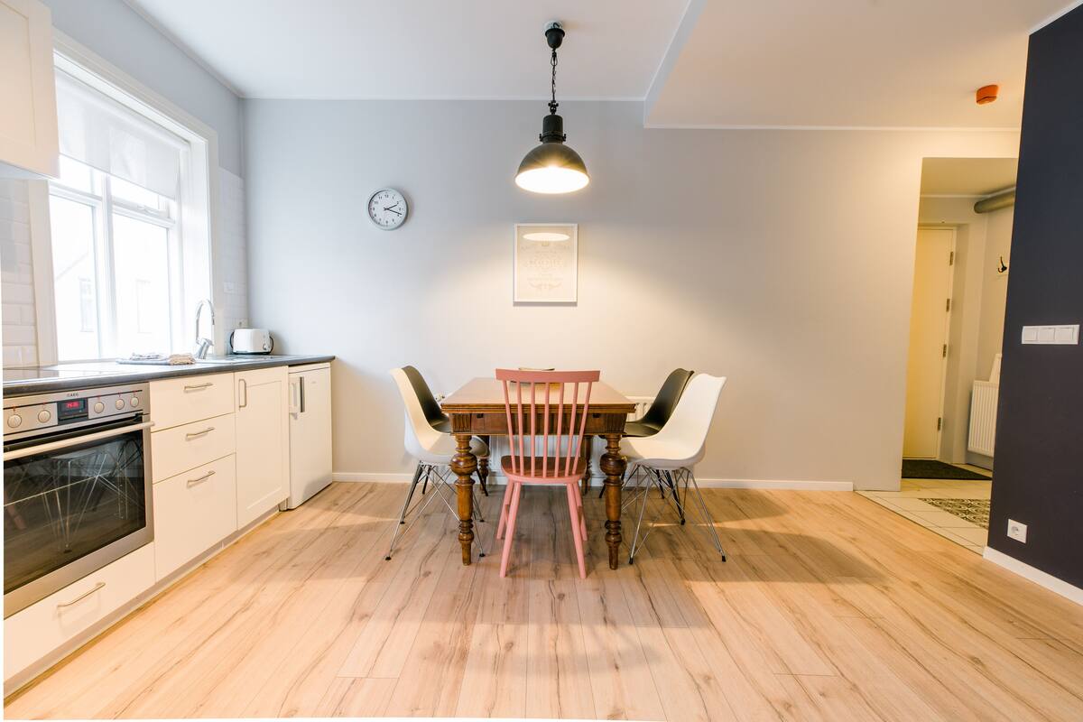 A modern kitchen with white cabinets, a wooden dining table, and a hanging light fixture.