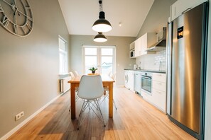 Een moderne keuken met een roestvrijstalen koelkast, een eettafel met stoelen en een hanglamp.