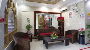 A reception area with wicker furniture, a red sofa, a coffee table, and a flower arrangement. - Cosy Inn (Miri)