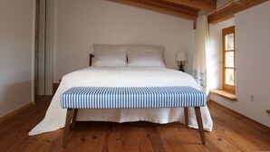 Een slaapkamer met een houten plafond, een bed met een gestreept dekbedovertrek, een bedlampje en een raam met gordijnen.