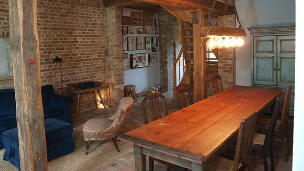 Een rustieke eethoek met een houten tafel en stoelen, een bakstenen muur en een hangende lamp.