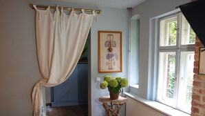 Een kamer met een raam, een radiator, een klein tafeltje met een plant en een gordijn.