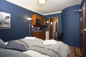 Pieni hotellihuone, jossa on sänky, pieni keittokomero, ruokapöytä ja tuoli.