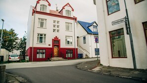 A two-story building with a red and white facade, a visible entrance with a red door, and a sign reading "Grundstiger."