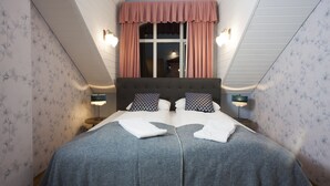 A bedroom with a large bed, two bedside tables, a window with curtains, and wall-mounted lights.