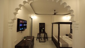 A bedroom with a four-poster bed, a TV mounted on the wall, and a small desk with a chair. - Rangmahal Pushkar by DIV Hospitality (Pushkar)