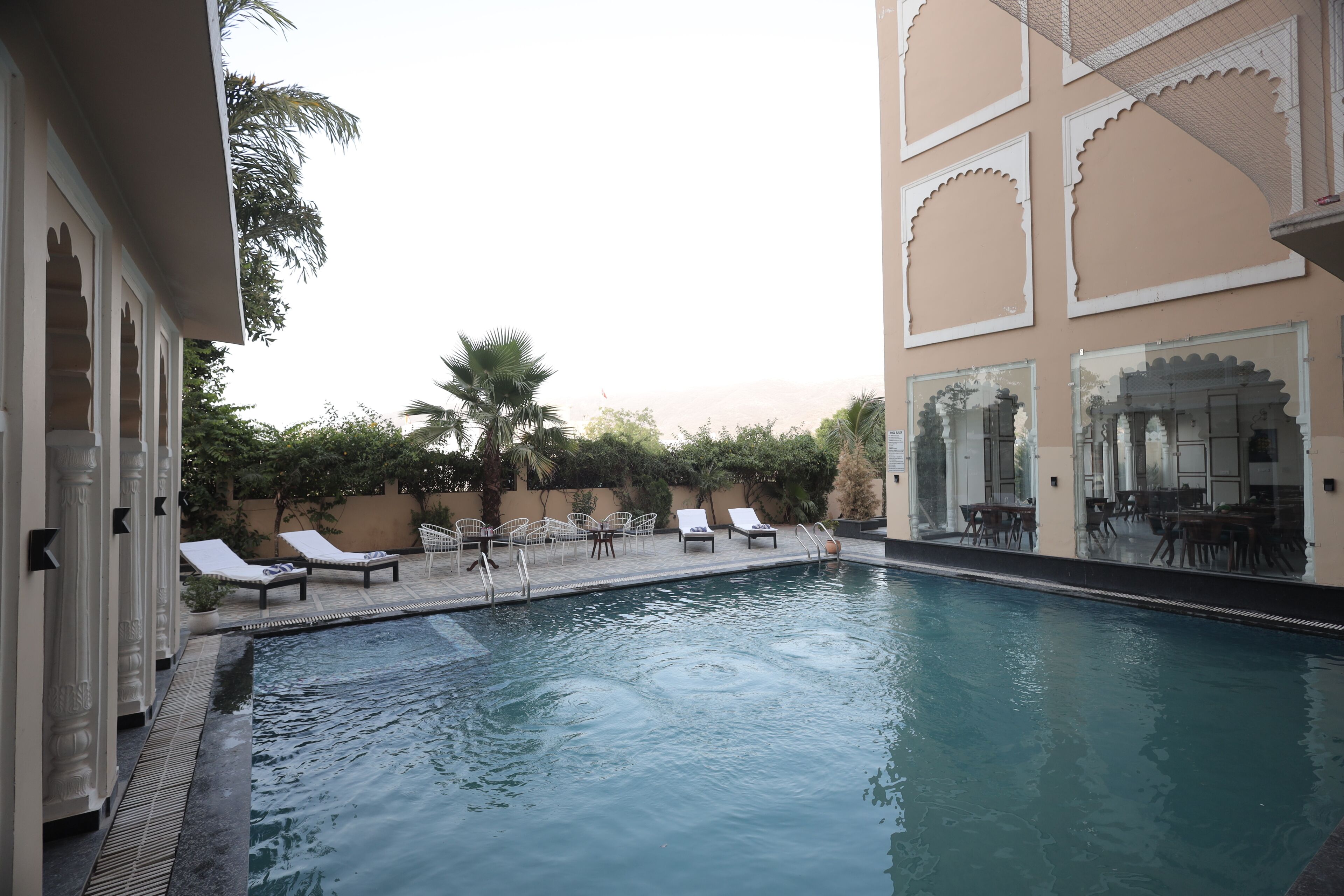 Una piscina con sillas de descanso, un comedor y un edificio con elementos arquitectónicos tradicionales.