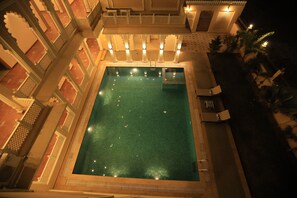 A rectangular swimming pool surrounded by ornate white railings and columns, with a view of a building with patterned walls and a balcony. - Rangmahal Pushkar by DIV Hospitality (Pushkar)