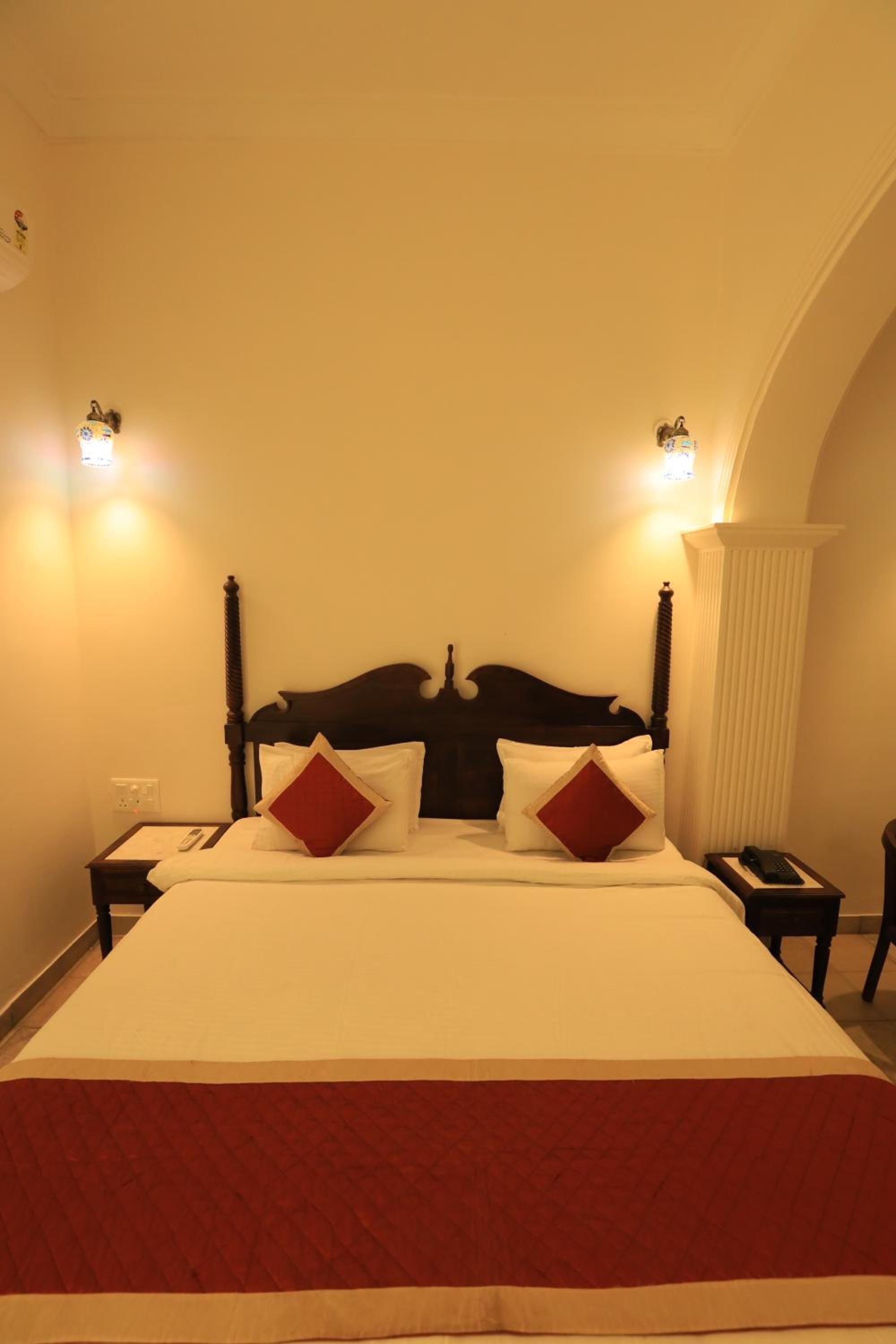 A hotel room with a large bed, two bedside tables, and two wall-mounted lamps.