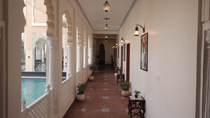 A corridor with arches, potted plants, and a pool view. - Rangmahal Pushkar by DIV Hospitality (Pushkar)