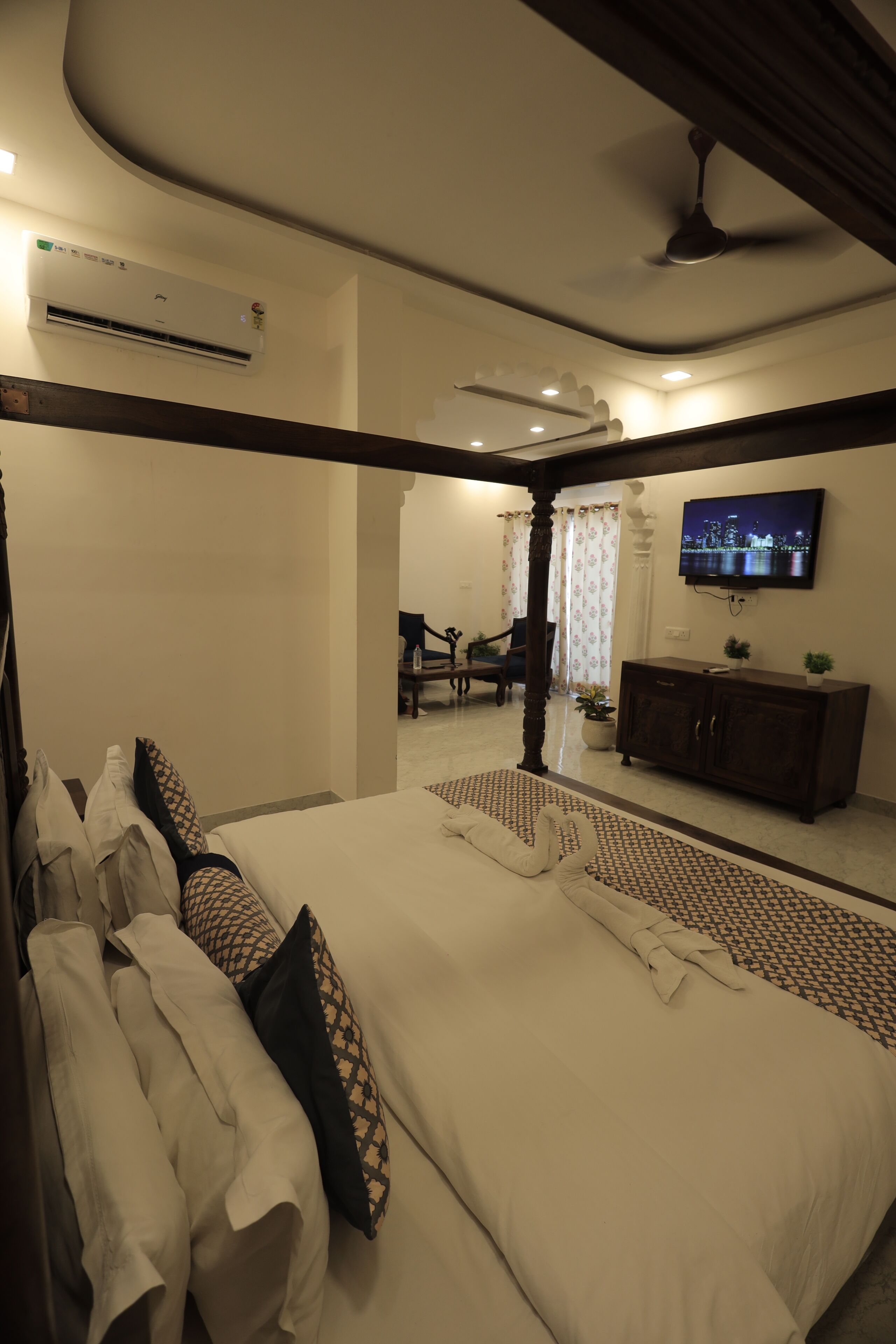 A hotel room with a bed, a television mounted on the wall, and an air conditioning unit.