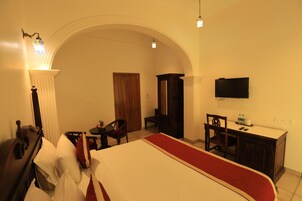 Una camera d'albergo con un letto, una scrivania, una sedia, un televisore e un arco.