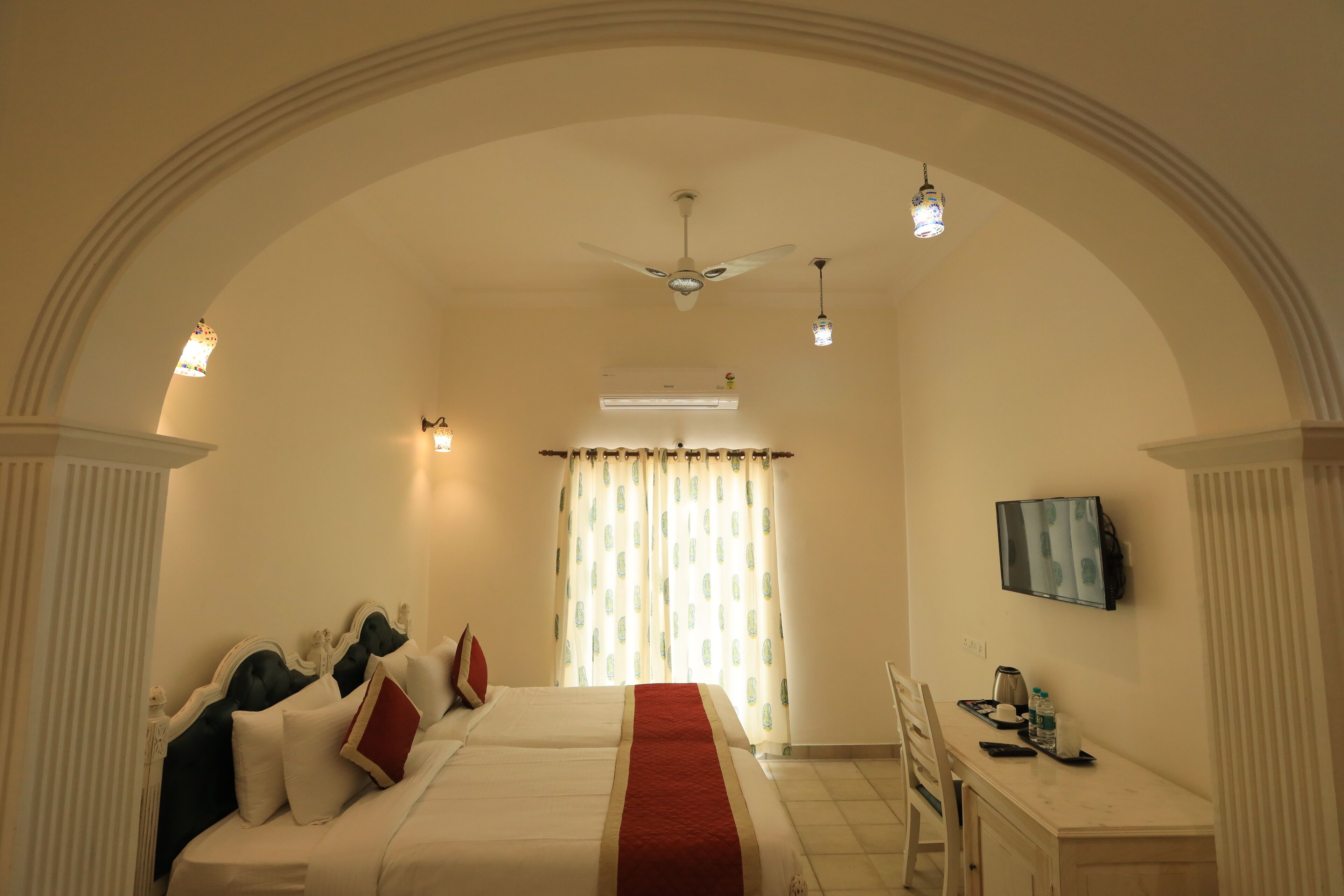 A hotel room with a large bed, a desk with a chair, a television, and a ceiling fan.