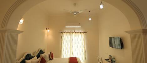 A hotel room with a large bed, a desk with a chair, a television, and a ceiling fan.