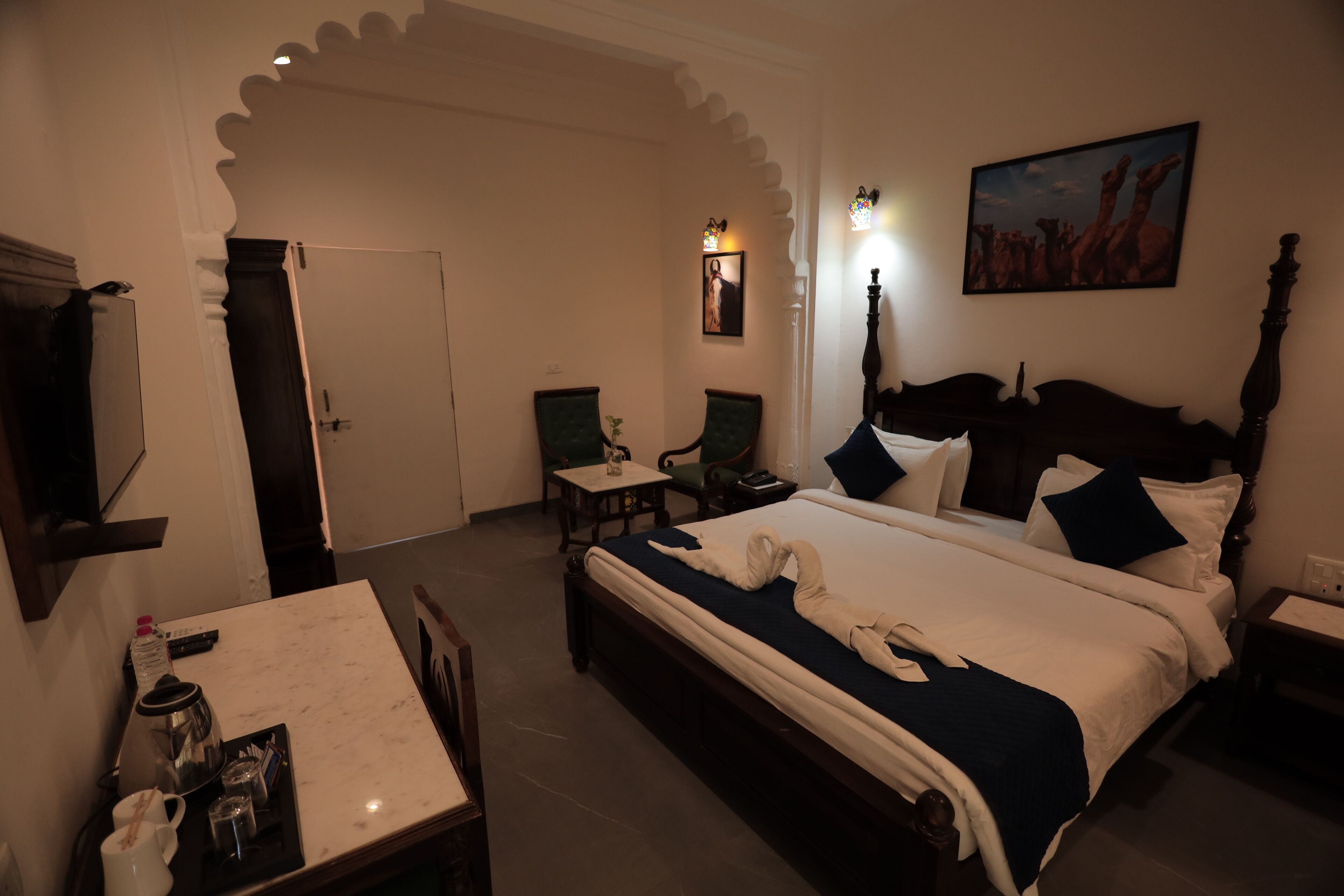 Una habitación de hotel con cama, escritorio con cafetera, silla y un cuadro en la pared.