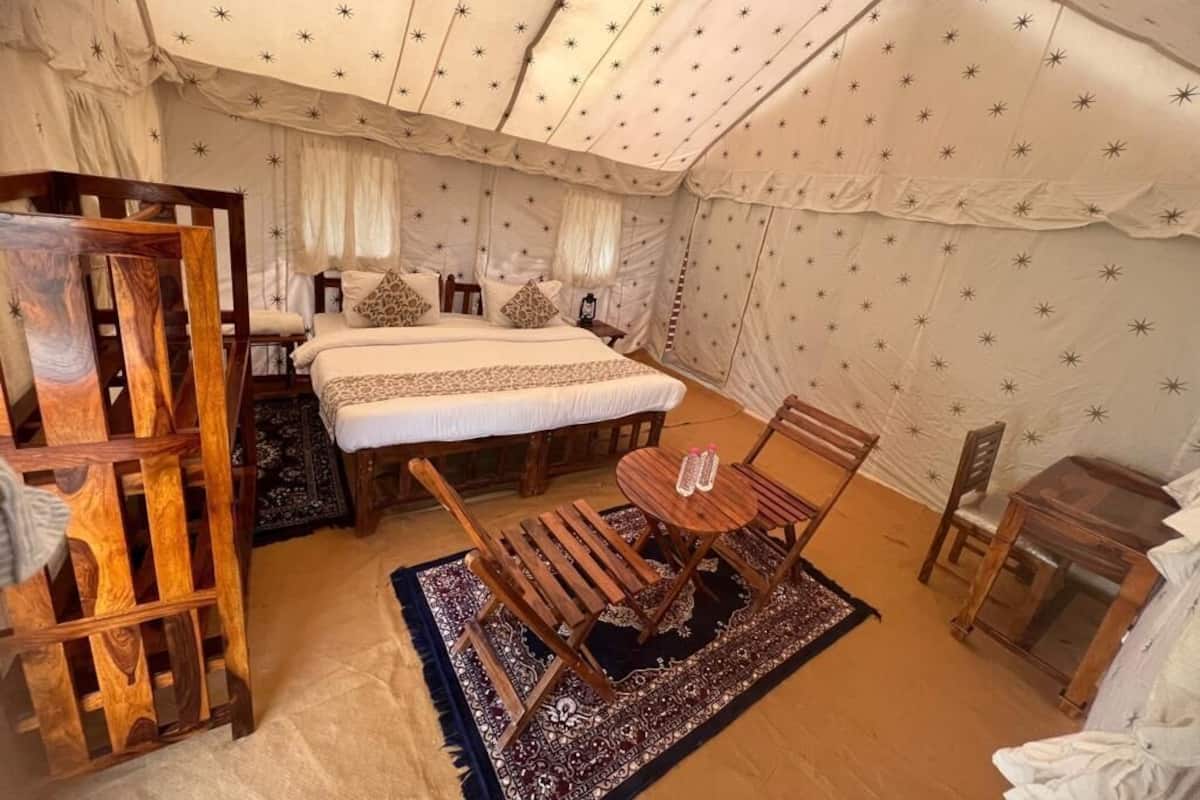 Una habitación con carpa, una cama, dos sillas de madera, una mesita y un armario.