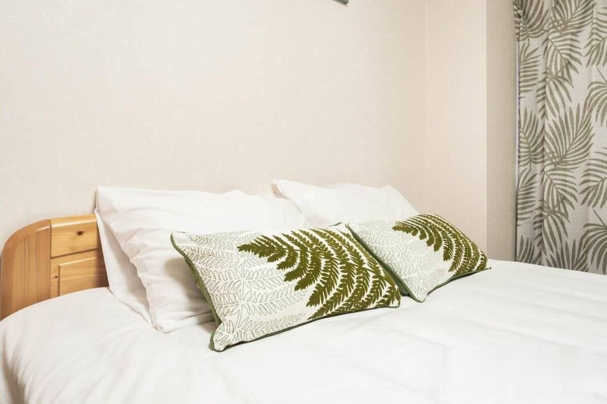A bed with white bedding and two pillows with a fern leaf pattern.