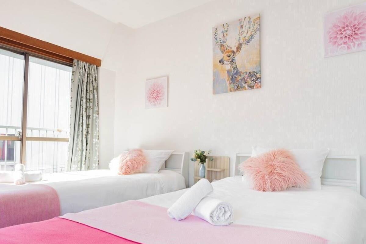 A hotel room with two beds, a large window, and artwork on the walls.