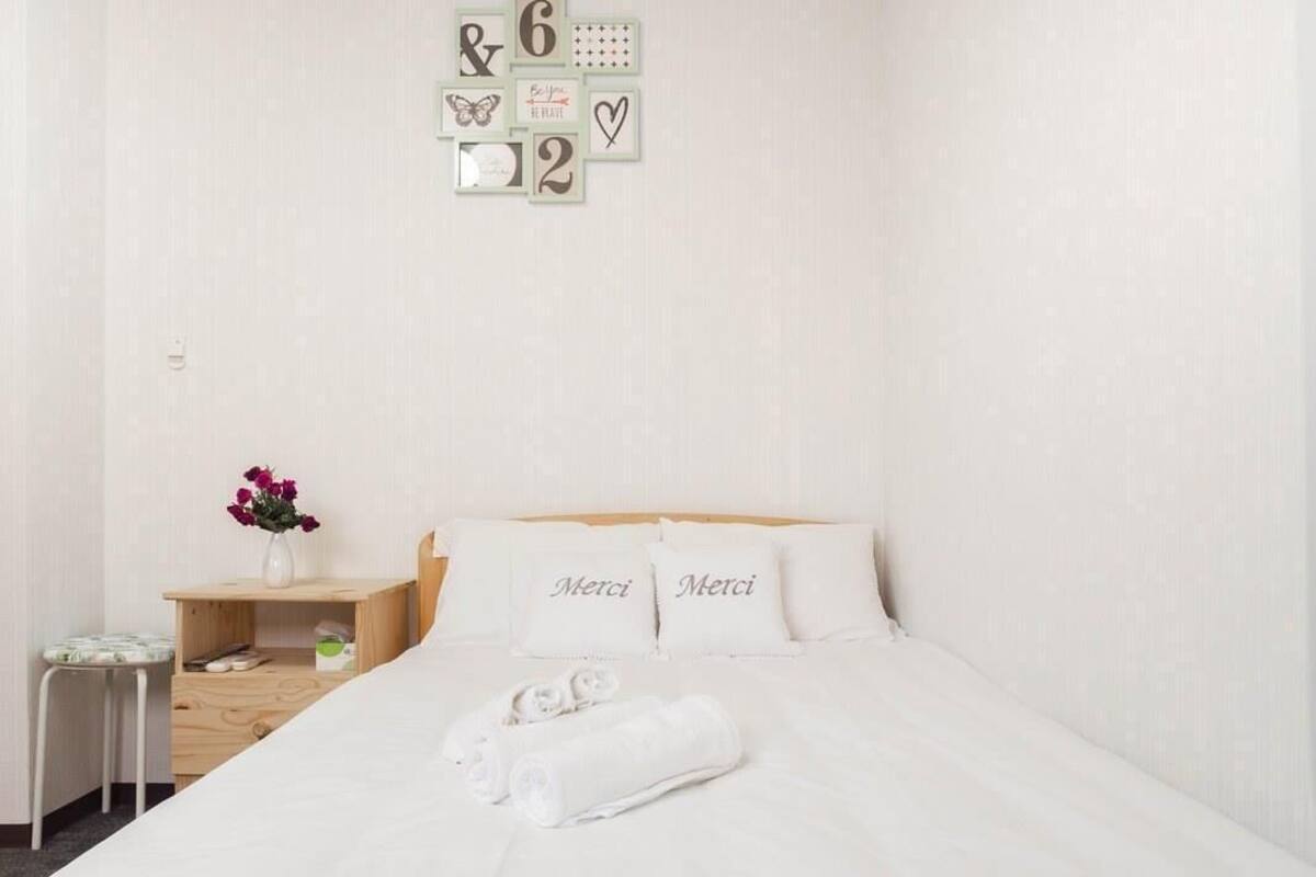A neatly arranged hotel room with a bed, a small wooden nightstand, a vase with flowers, and a wall with decorative items.