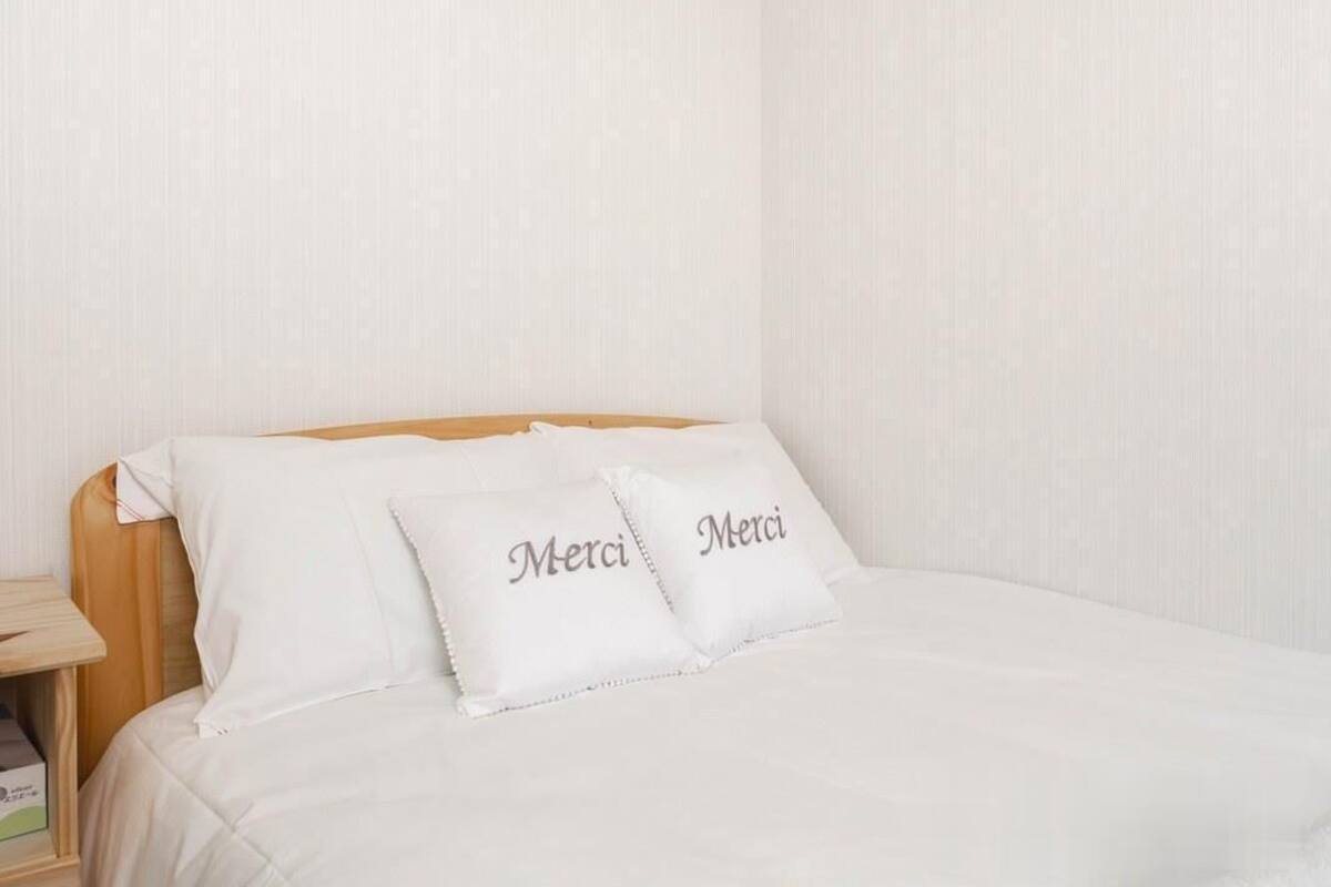 A neatly made bed with white bedding and two pillows with the word "Merci" on them.