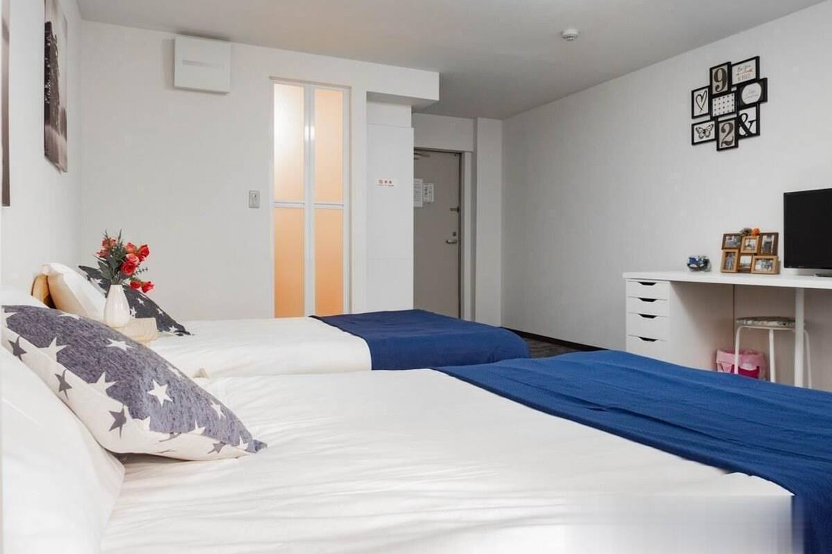 A hotel room with two beds, a desk, and a chair. There is a door leading to a bathroom and a closet.