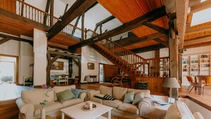 Un vaste espace de vie doté d’un haut plafond en bois, d’un escalier et d’un coin salon confortable.