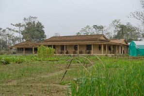 A two-story building with a tiled roof, a porch with multiple chairs, and a green field in the foreground.