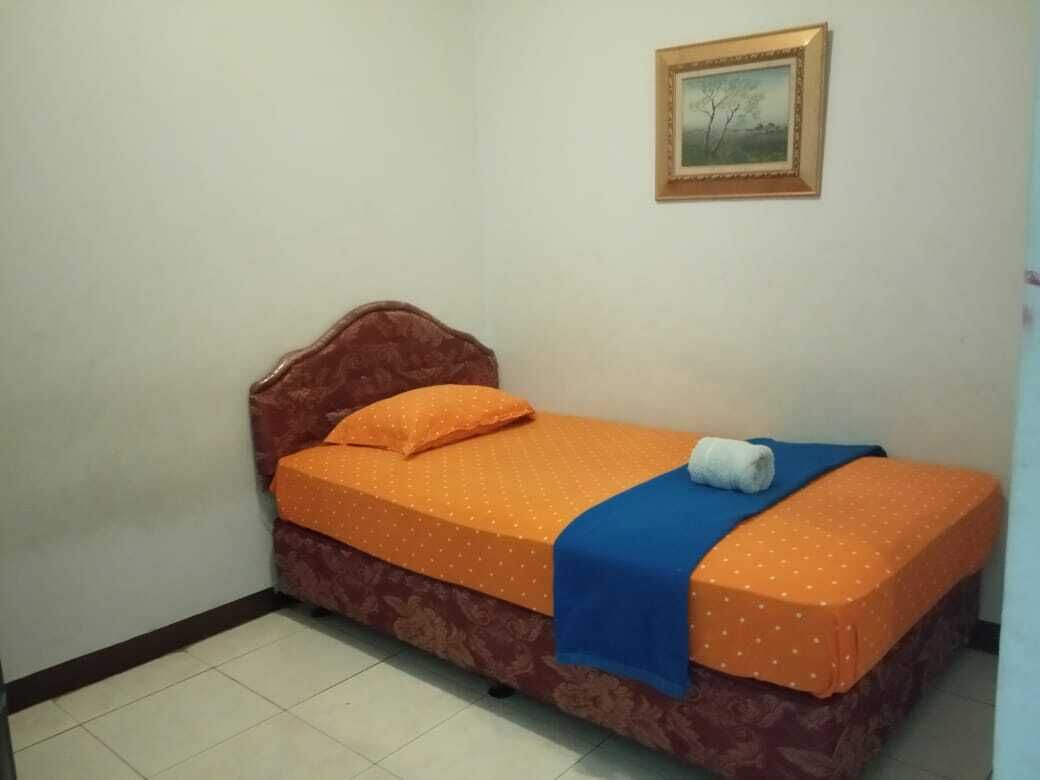 A single bed with an orange bedspread and a blue blanket, a wooden headboard, and a framed picture on the wall.