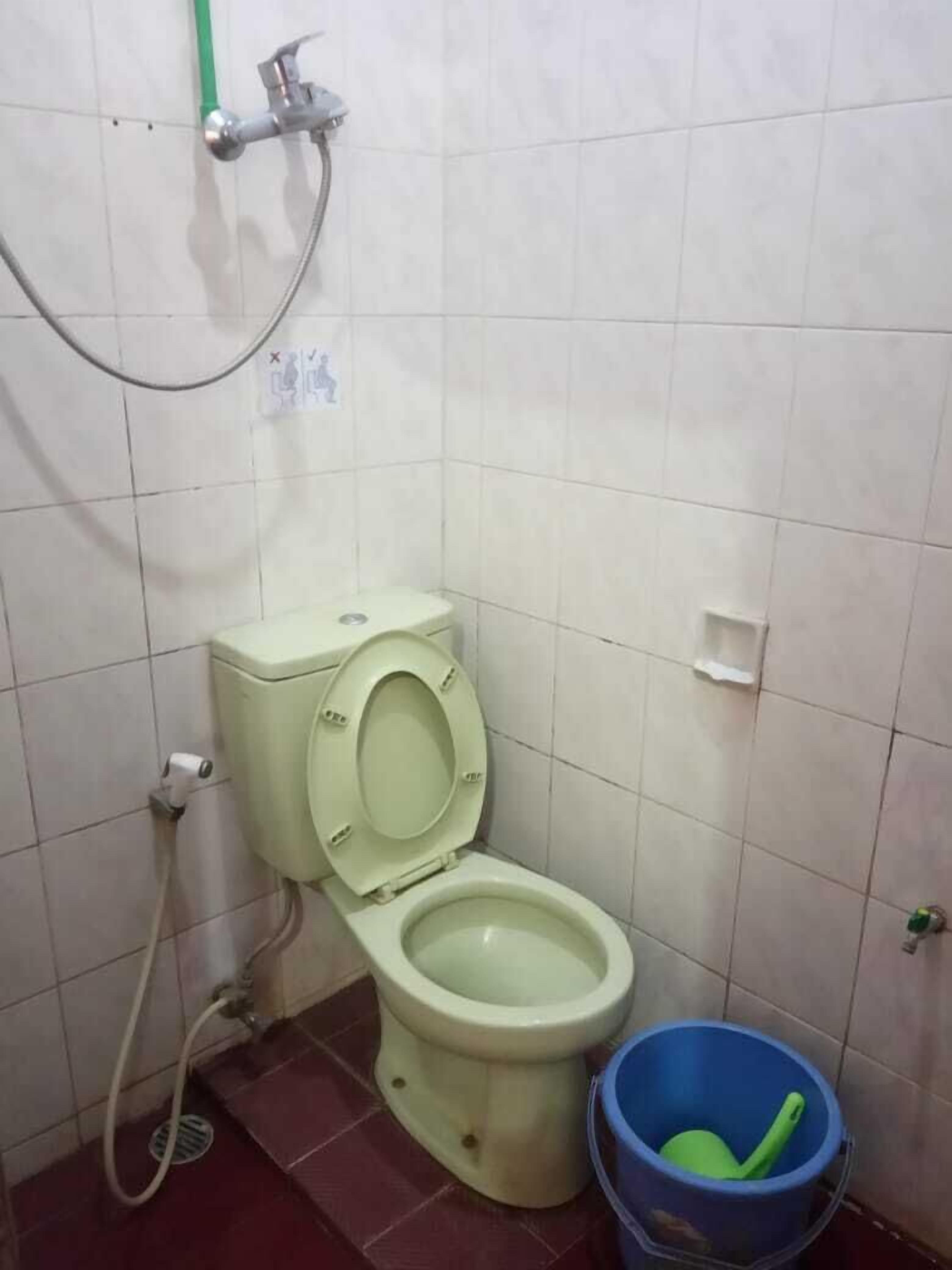 A small, basic bathroom with a toilet, a shower, and a blue bucket.