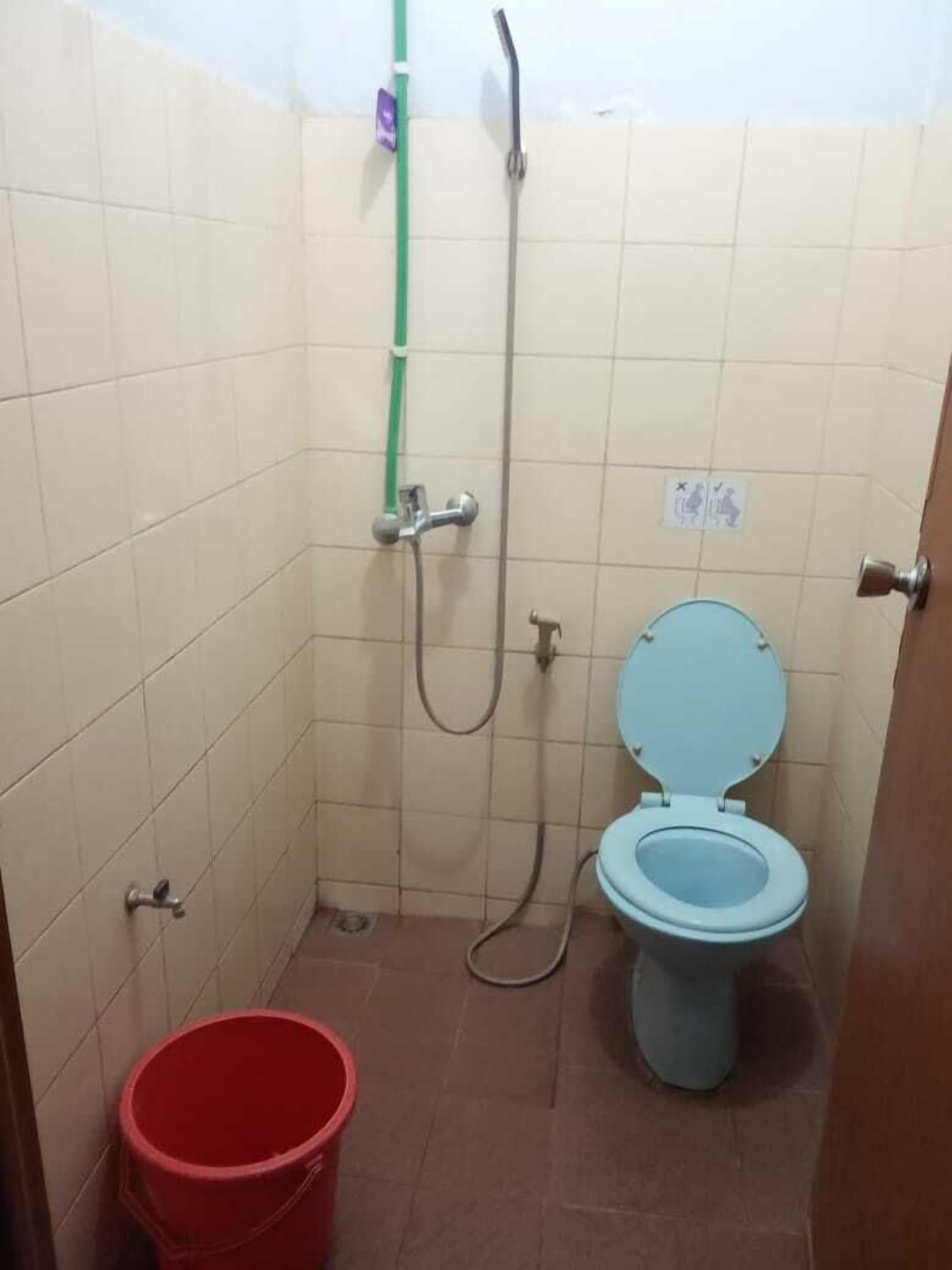 A small bathroom with a toilet, a shower, and a red bucket.