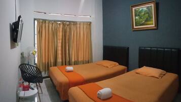 Habitación de hotel con dos camas individuales, una mesita con una silla, un televisor montado en la pared y una ventana con cortinas.