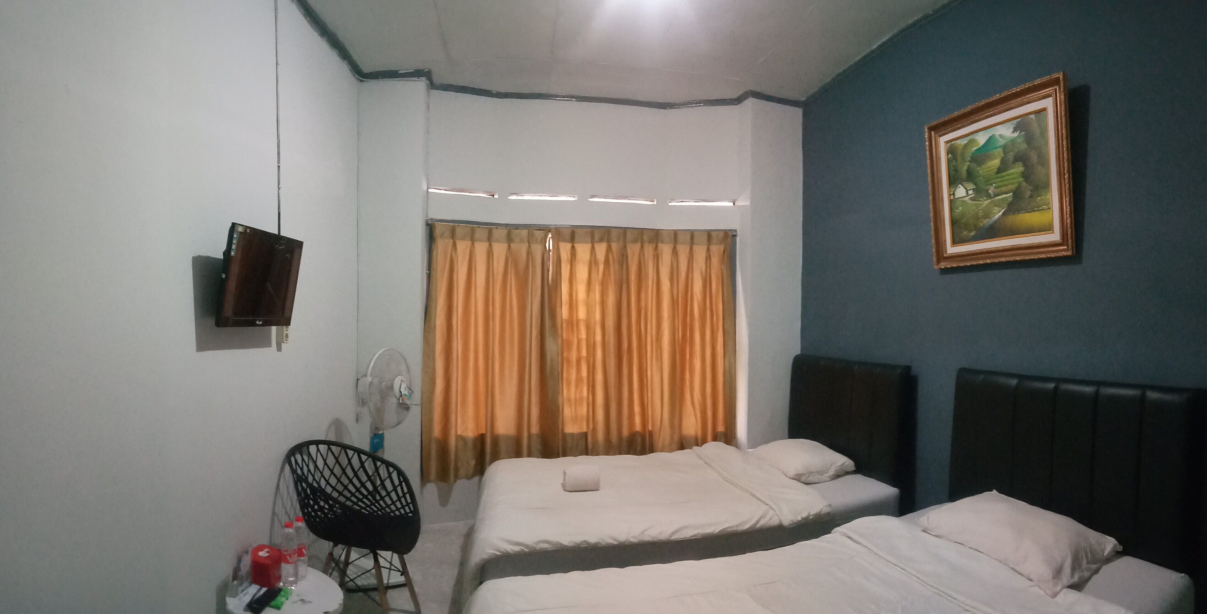 A hotel room with two beds, a TV mounted on the wall, a fan, and a painting.