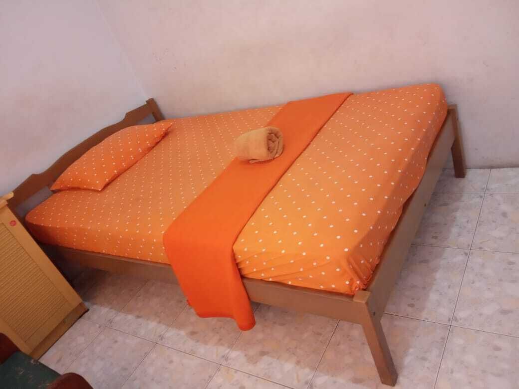 A single bed with an orange bedspread and pillows, a wooden frame, and a small bedside table.