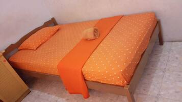 A single bed with an orange bedspread and pillows, a wooden frame, and a small bedside table.