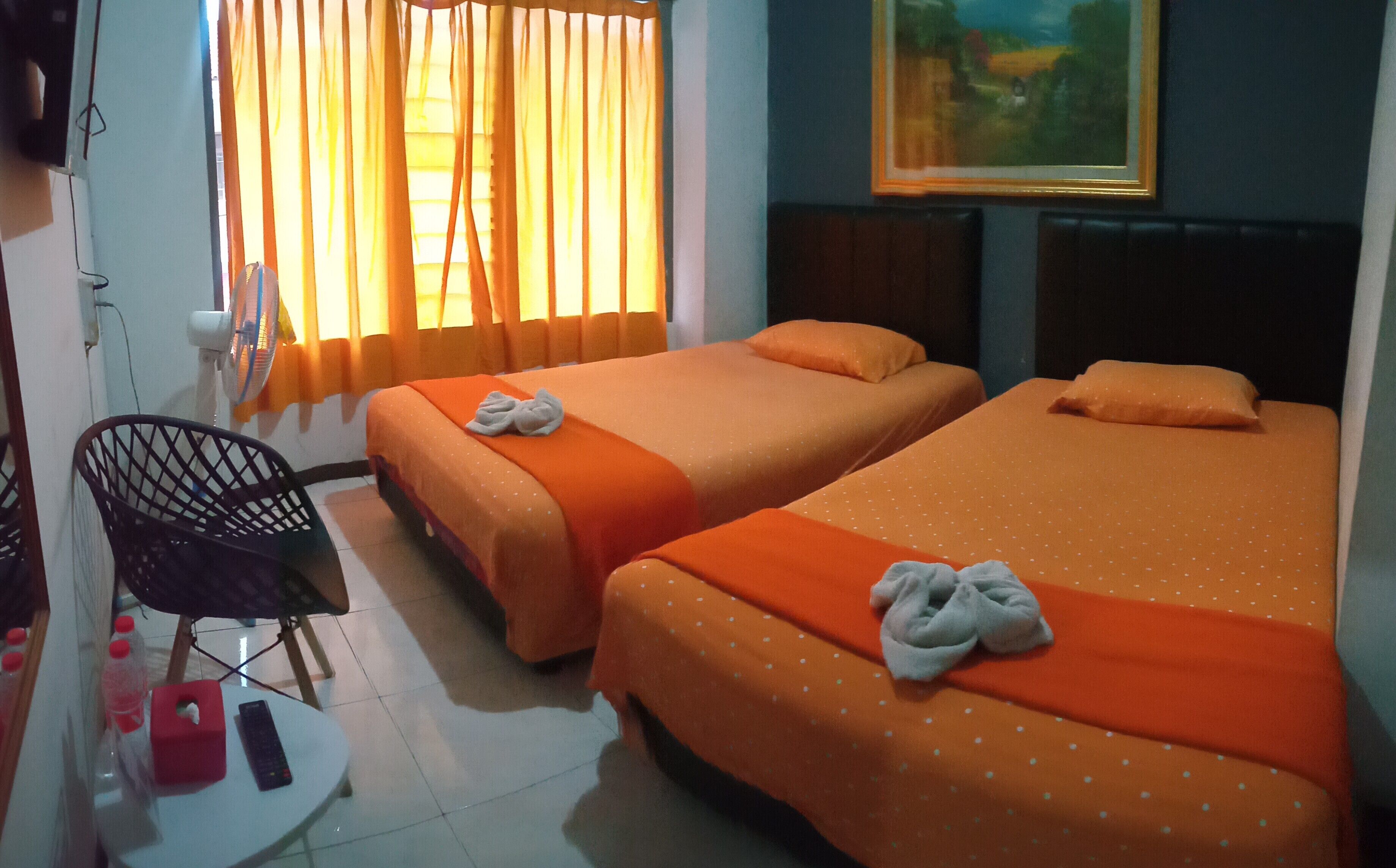 A hotel room with two beds, a chair, a small table with a remote control, and a painting on the wall.