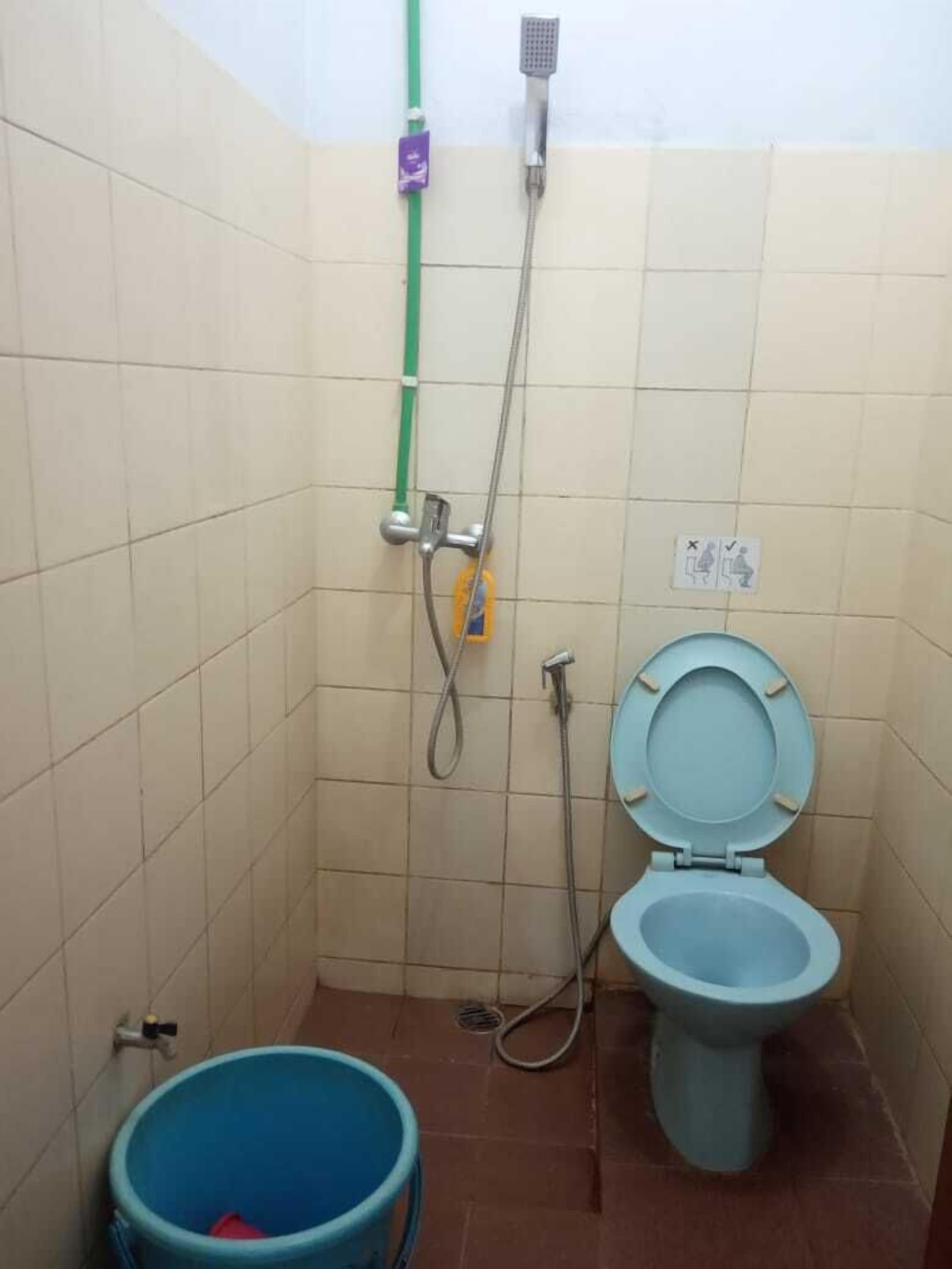 A small bathroom with a toilet, a shower, and a blue bucket.
