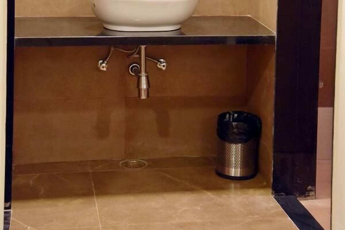 A bathroom with a white sink, a mirror, and a trash can.