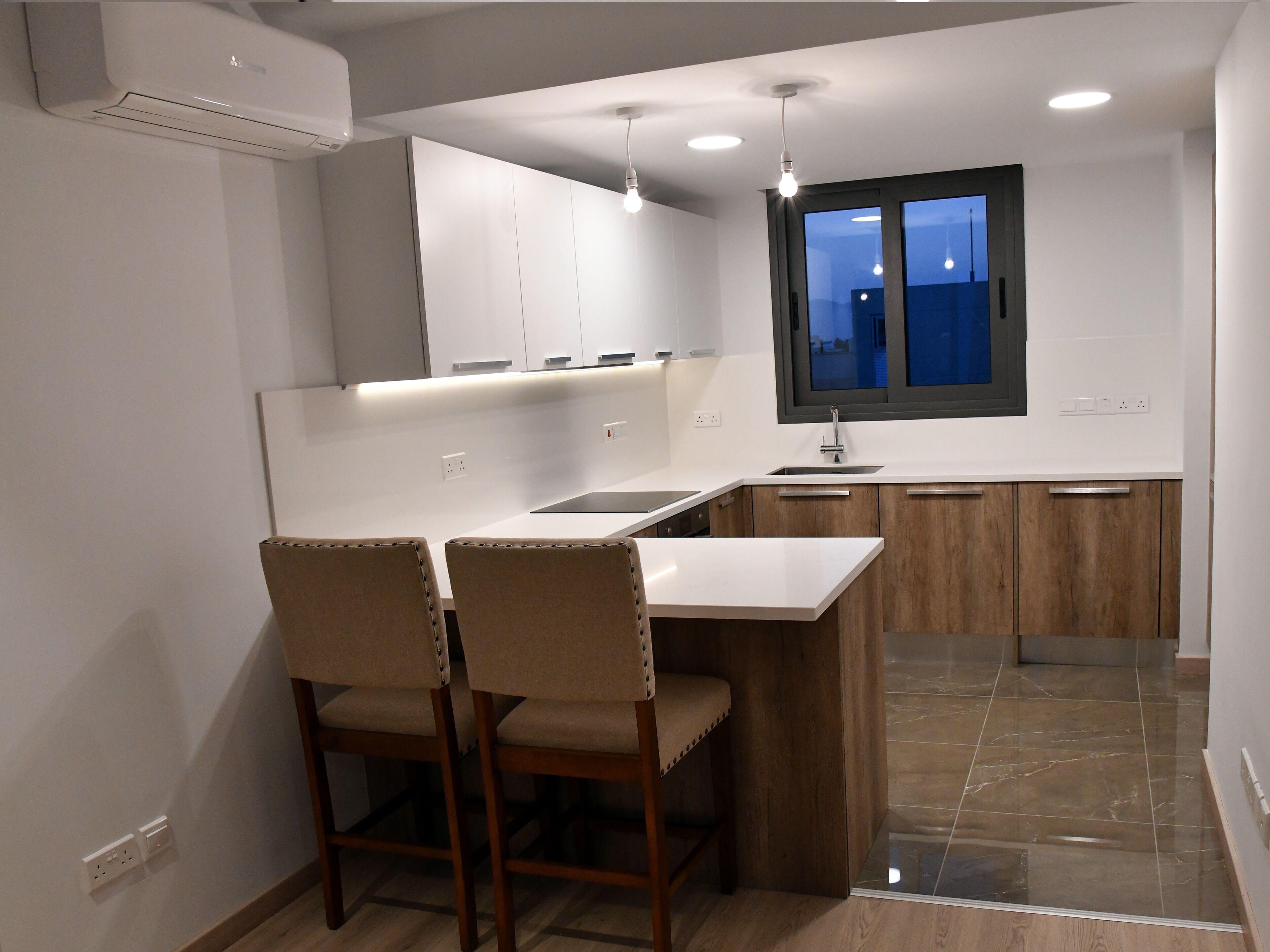 A modern kitchen with a central island, two bar stools, wooden cabinets, and a window with a view.