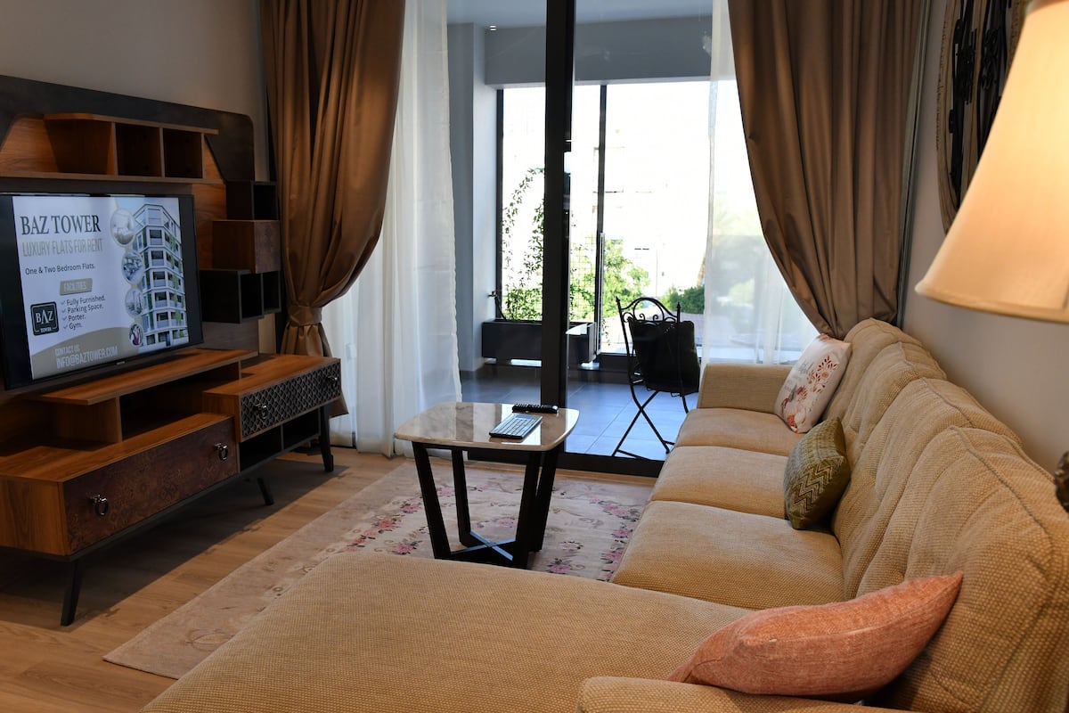 A living room with a sofa, a coffee table, and a TV displaying a property advertisement.