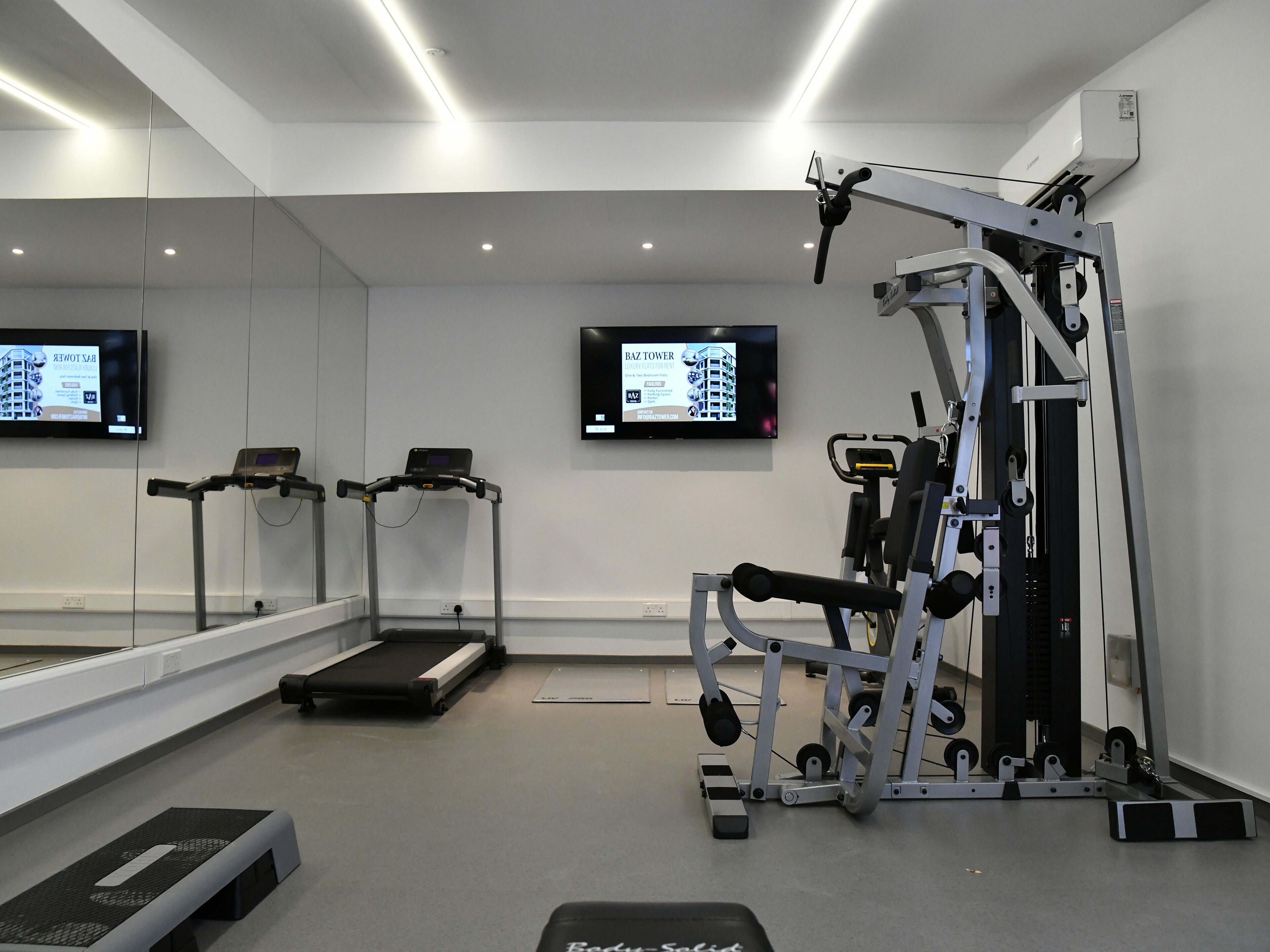 A gym with treadmills, a weight machine, and a mirrored wall.