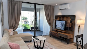 Uma sala de estar com sofá, mesa de centro, televisão e luminária.